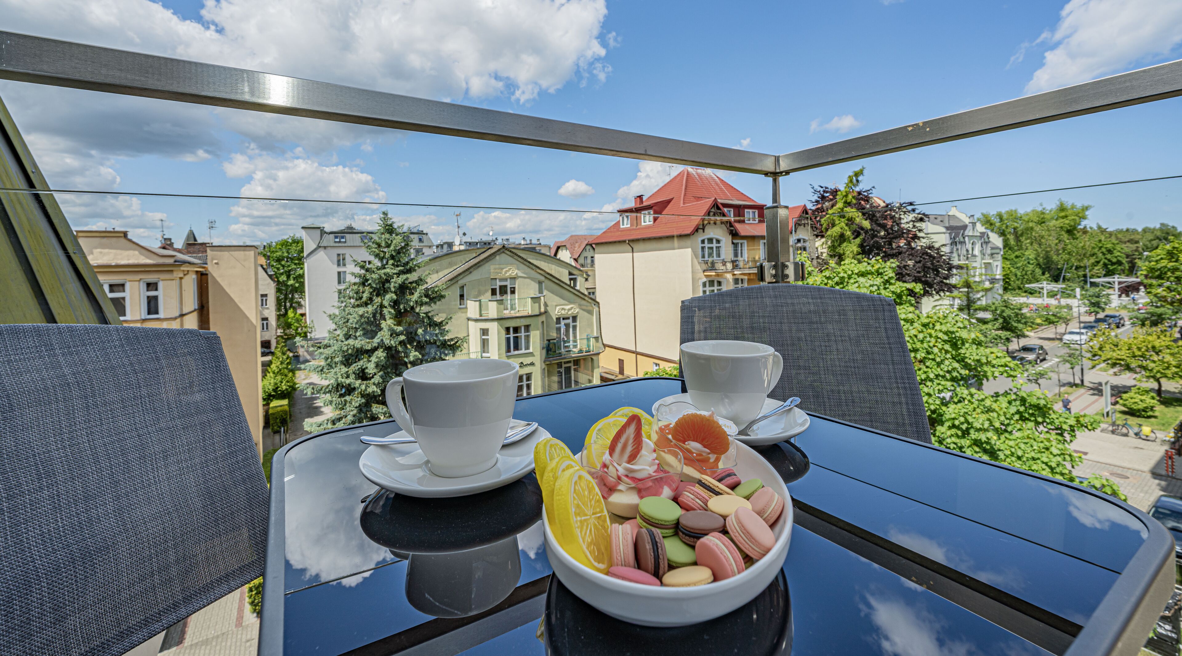 A balcony table with two white cups, a bowl of macarons, and lemon slices.