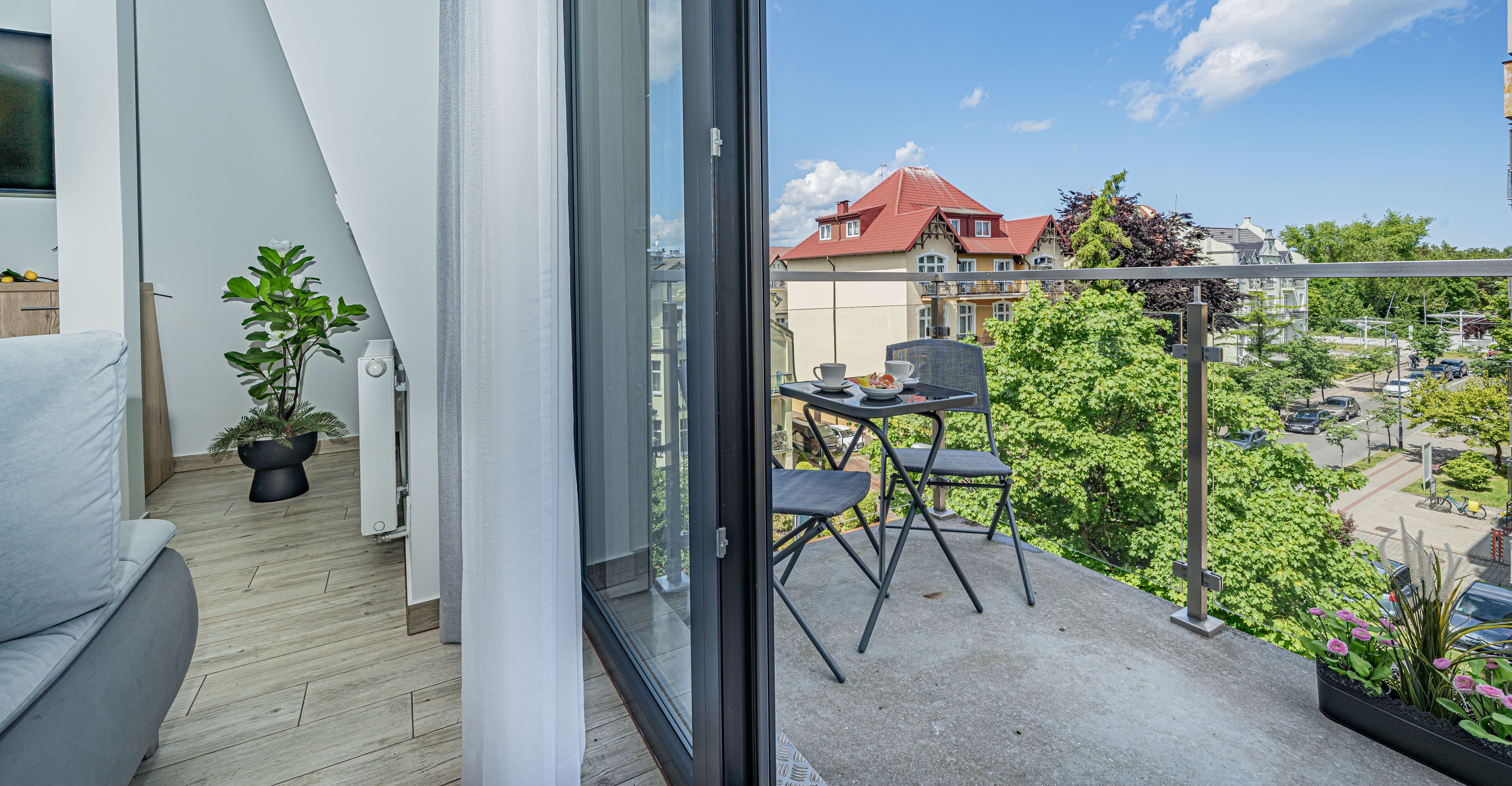 Un balcone con divano, un tavolino e sedie, affaccia su una zona residenziale con case e vegetazione.