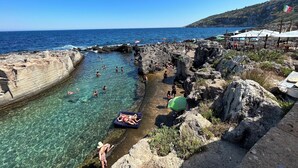 A rocky coastal area with clear water, people swimming and relaxing, and a restaurant with outdoor seating. - Seafront historical villa with fabulous garden and private pool (Marina Serra)