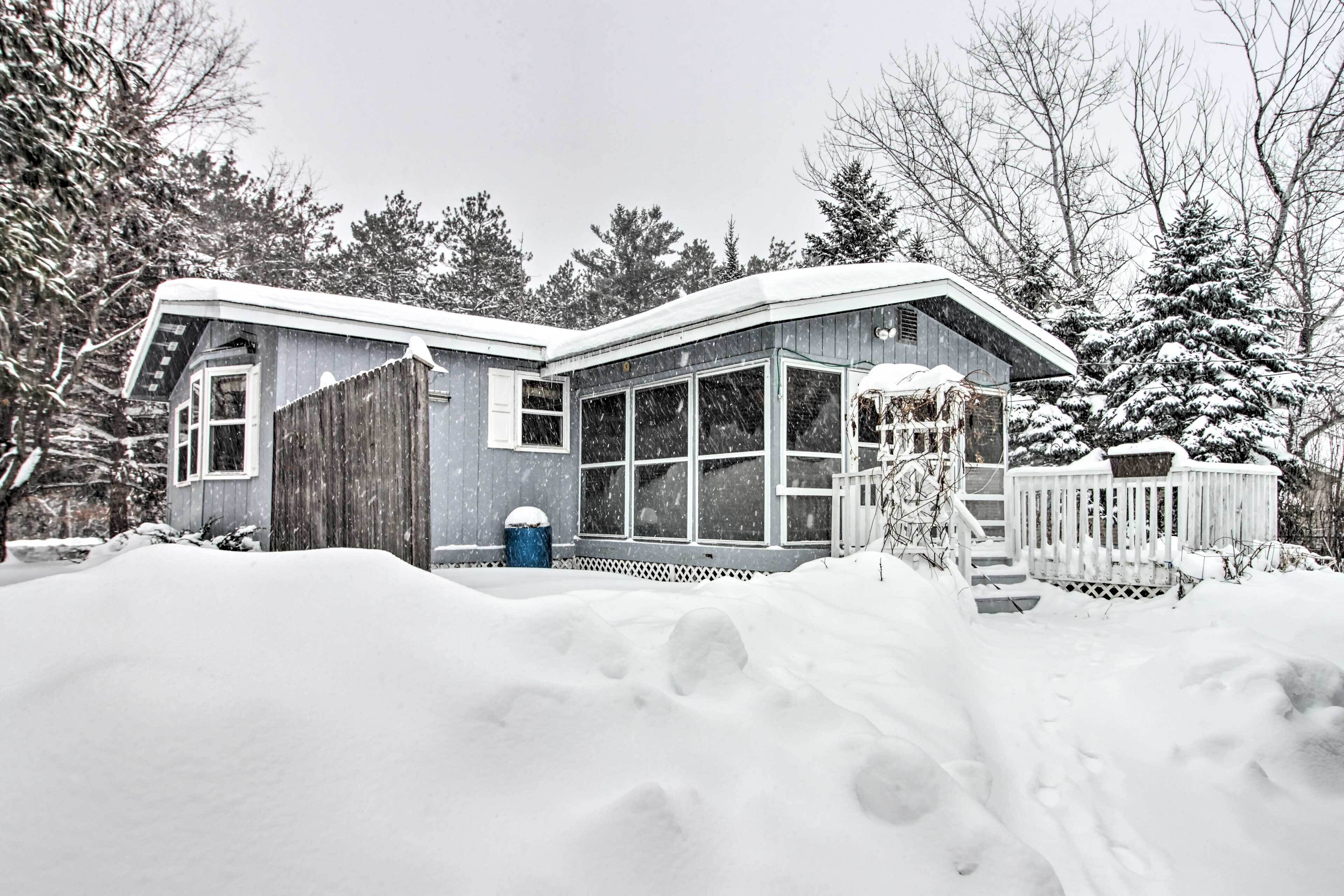 Une maison avec une grande façade vitrée, une terrasse en bois et une cour enneigée.