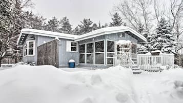 Une maison avec une grande façade vitrée, une terrasse en bois et une cour enneigée.