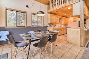 A dining area with a table set for four, wooden cabinets, and a view of the outdoors through large windows.