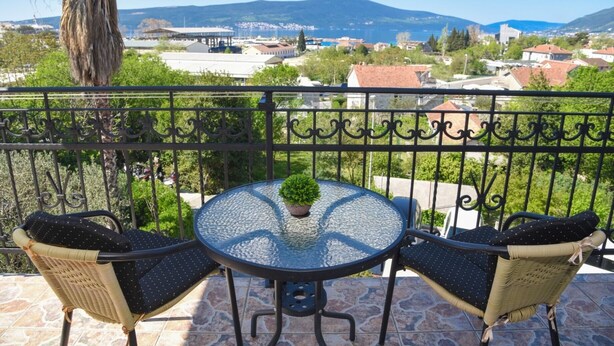 Ein Balkon mit zwei Korbstühlen und einem runden Tisch, mit Blick auf eine malerische Stadt- und Berglandschaft.