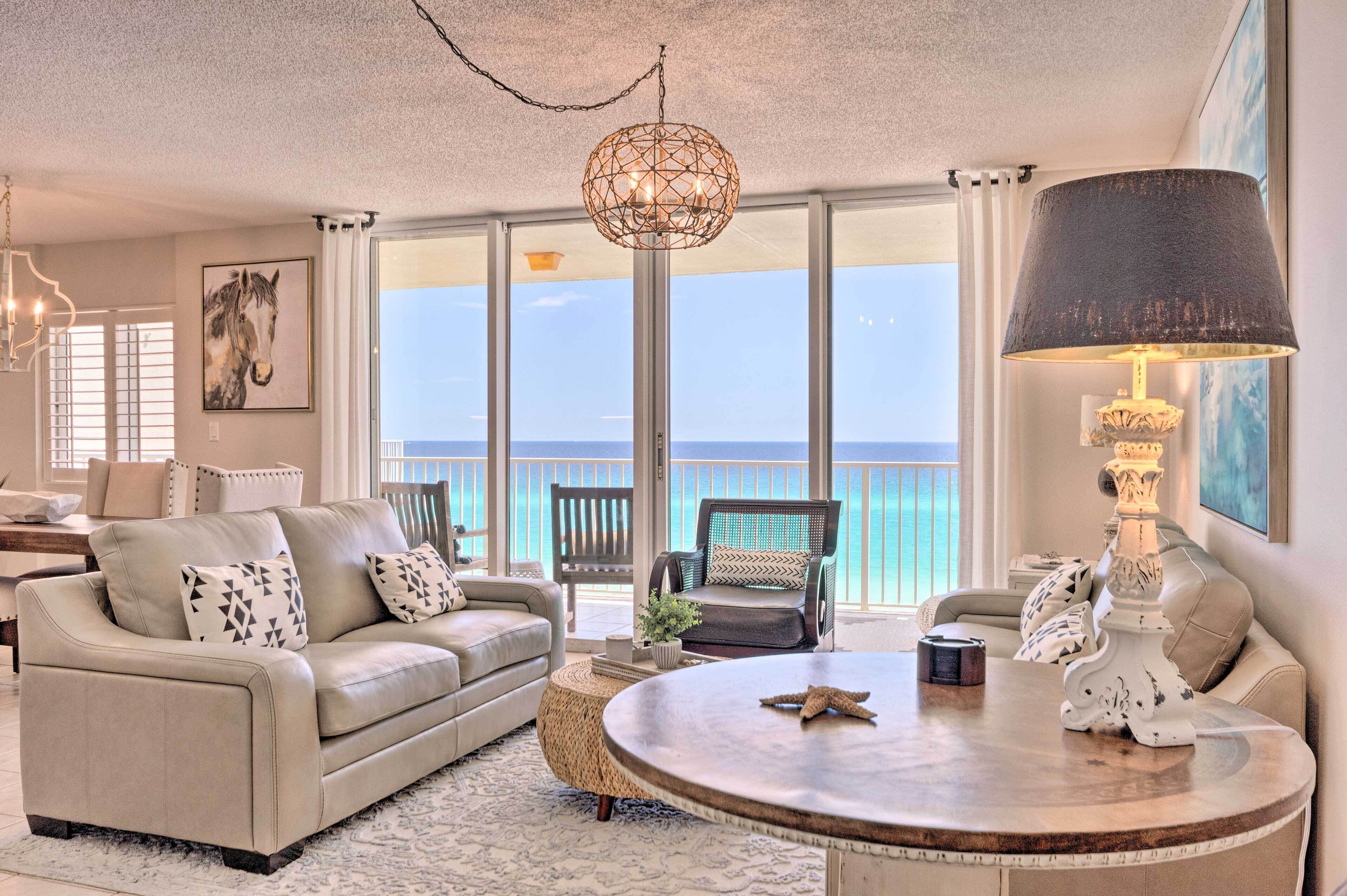 A spacious living room with a large window offering a view of the ocean, a round coffee table, and comfortable seating.