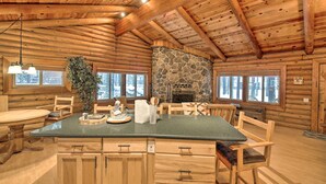 A log cabin interior with a stone fireplace, wooden furniture, and large windows. - 11 Mi to Rainbow Lake: Family Home w/ Large Yard (Pinetop)