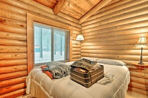 A log cabin bedroom with a bed, a window with blinds, a lamp on a side table, and a suitcase on the bed. - 11 Mi to Rainbow Lake: Family Home w/ Large Yard (Pinetop)