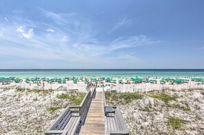 A beach with a wooden boardwalk leading to the shore, surrounded by beach umbrellas and people. - Steps to Sand! Miramar Unit w/ Pool, Tennis & More (Miramar Beach)