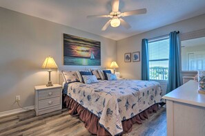 A bedroom with a bed, nightstands, a ceiling fan, a painting of a sailboat, and a window with curtains. - Steps to Sand! Miramar Unit w/ Pool, Tennis & More (Miramar Beach)