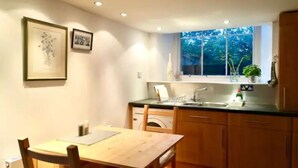 A compact kitchen with wooden cabinets, a sink, and a window overlooking greenery. - Central Mezzanine Apartment in Historic School (Edinburgh)