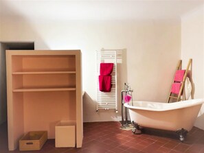 A bathroom with a freestanding bathtub, a white radiator, and a wooden shelf unit.