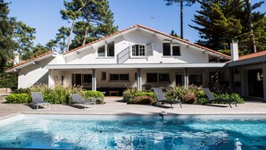 Ein zweistöckiges Haus mit Swimmingpool, umgeben von Bäumen und mit rotem Ziegeldach.
