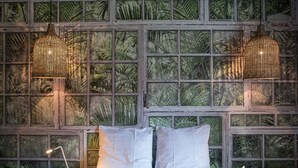 Ein Zimmer mit einem Bett, zwei Pendelleuchten und einem Fenster mit tropischem Wandpapier.