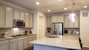 A modern kitchen with light-colored cabinets, stainless steel appliances, and a granite countertop.