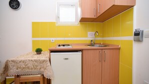 Una cocina compacta con un refrigerador pequeño, un lavamanos y una ventana con persianas.