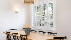 A dining area with a wooden table and black chairs, a woven pendant light, and a window with blinds. - 4 bedrooms in one of the most popular + charming neighborhoods in Arcadia (Phoenix)