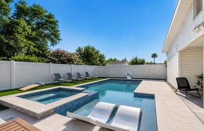 Un jardin avec une piscine rectangulaire, un panier de basketball et plusieurs chaises longues.