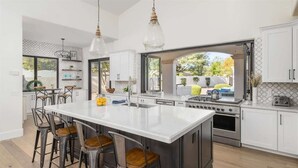 Cozinha moderna com uma ilha grande, banquetas, eletrodomésticos de aço inoxidável e iluminação pendente.