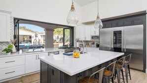Cozinha moderna com uma ilha grande, eletrodomésticos de aço inoxidável e vista para o exterior.