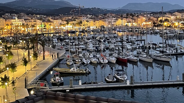 Marina con numerosas embarcaciones amarradas, rodeada de edificios y un paisaje montañoso.