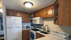 A kitchen with wooden cabinets, a white refrigerator, a microwave, a stove, a sink, and a dish rack. - Spacious, comfortable 2 bedroom oceanfront condo with free WiFi, an outdoor pool, and an enclosed balcony with a great ocean view located midtown only steps to the beach! (Ocean City)