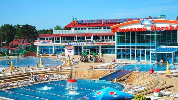 Un área de piscina al aire libre con varias piscinas, un restaurante y un edificio grande con techo rojo.