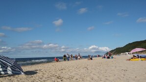 A beach with people walking and relaxing, umbrellas, and a tent.