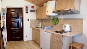A compact kitchen with a dishwasher, a sink, and a kettle. There is a wooden door and a fire extinguisher on the wall.