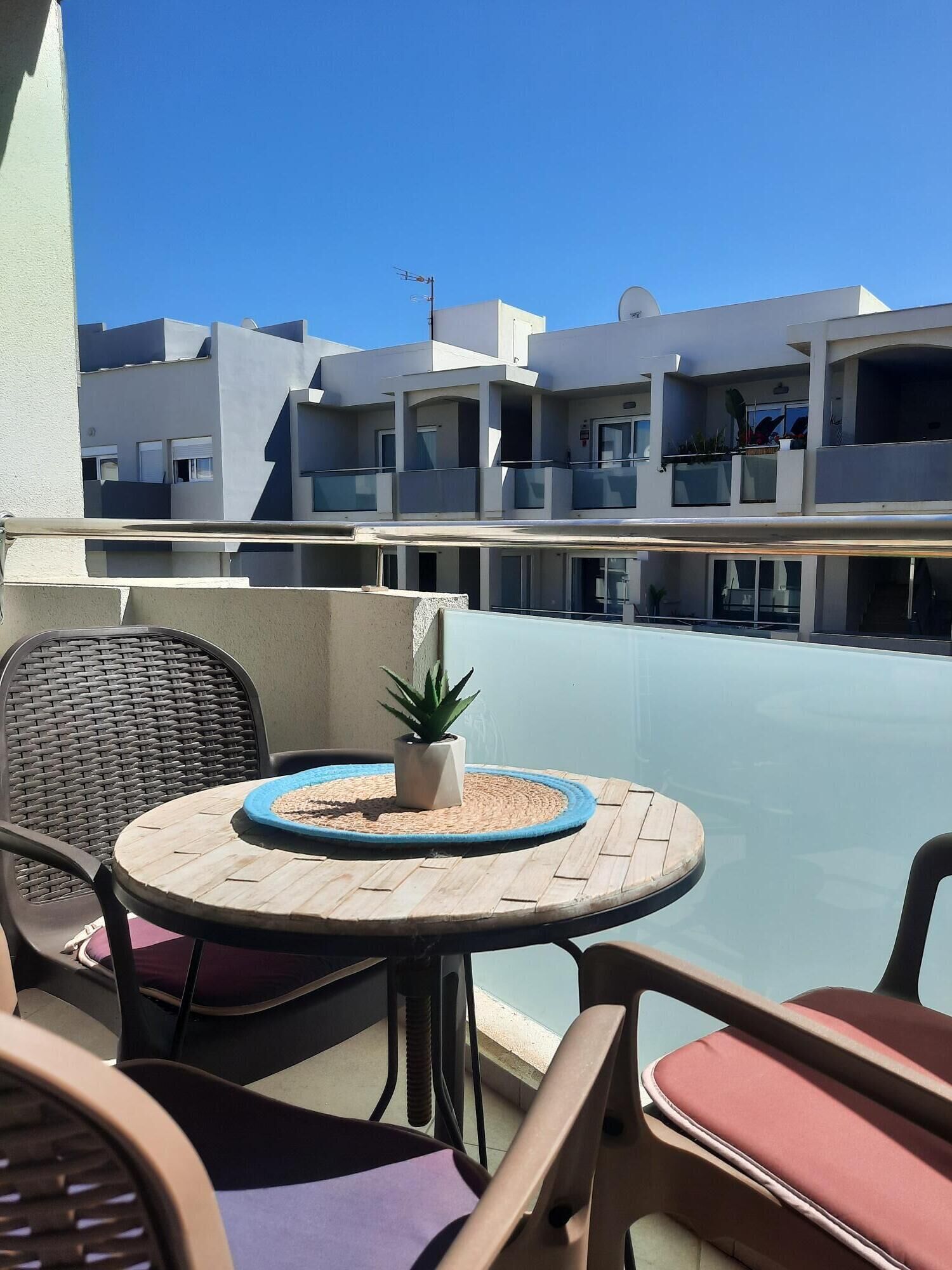 Ein Balkon mit rundem Tisch, Stühlen und einer Topfpflanze.