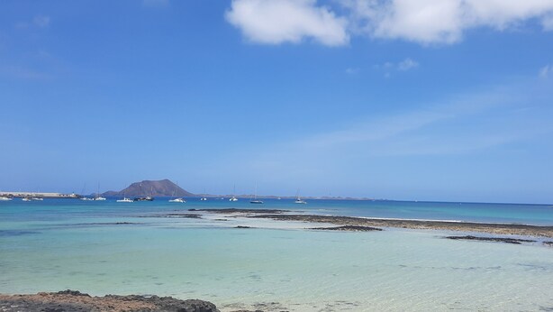 A coastal landscape with clear turquoise waters, rocky shorelines, and boats anchored in the distance.