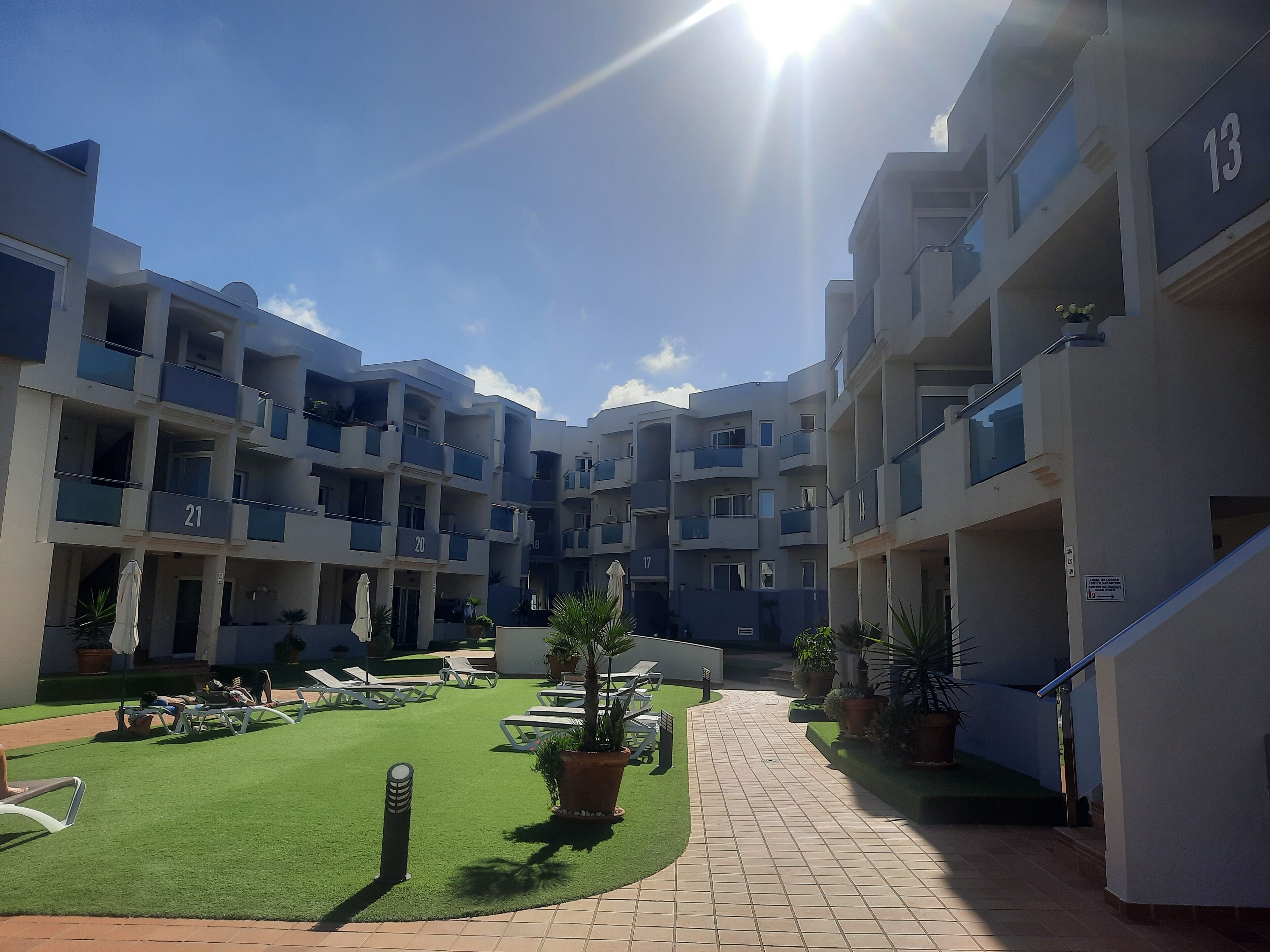 A courtyard with multiple balconies, a tiled pathway, and lounge chairs.