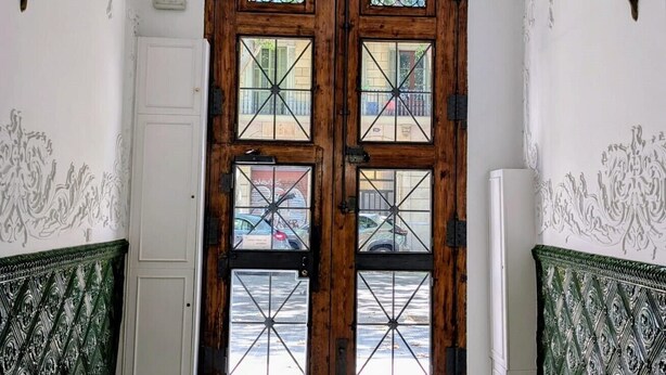 A hallway with ornate ceiling and a wooden door with glass panels. - Sunrise: Elegant 2BR/1BA in the Heart of Central Barcelona, Dreta de l'Eixample (Barcelona)