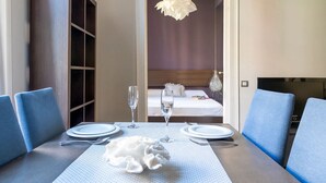 A dining area with a table set for two, a view into a bedroom with a bed and a nightstand, and a hanging light fixture above the table. - Sunrise: Elegant 2BR/1BA in the Heart of Central Barcelona, Dreta de l'Eixample (Barcelona)