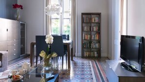 A modern living room with a glass coffee table, a bookshelf, a television, and a dining area with chairs and a table. - Sunrise: Elegant 2BR/1BA in the Heart of Central Barcelona, Dreta de l'Eixample (Barcelona)