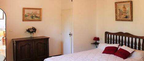 A bedroom with a large bed, a wooden headboard, a chandelier, a dresser, and two framed pictures on the walls.
