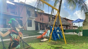 A playground with swings and a slide, surrounded by grass and buildings. - Your Beach House 3 min from Beach Park - Cs 01 (CE)