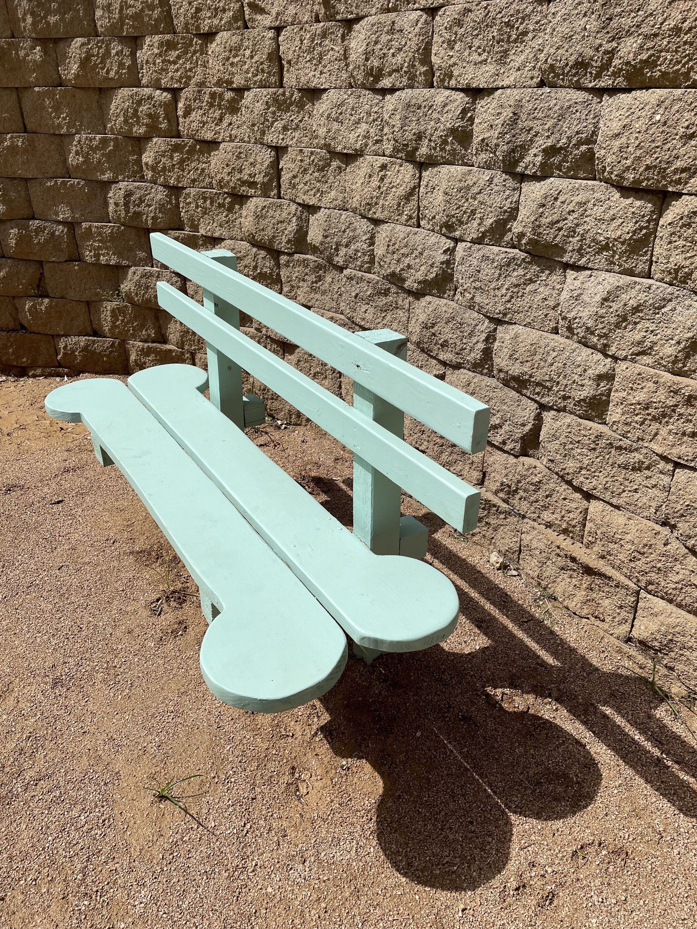 A light green picnic table with a stone wall in the background.