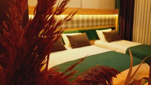 A hotel room with a bed, green and white bedding, a headboard with a patterned design, and a large decorative plant in the foreground. - Dinamik Otel (Sarikamis)