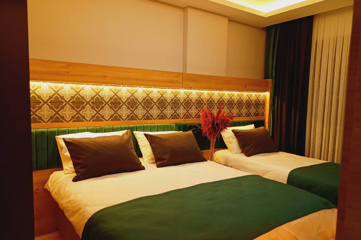 A hotel room with two beds, a wooden headboard with a geometric pattern, and a vase with red flowers.