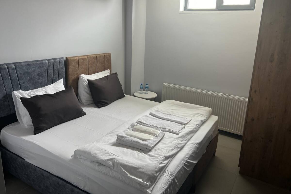 A neatly made bed with white linens and towels, a wooden headboard, and a small bedside table with water bottles.