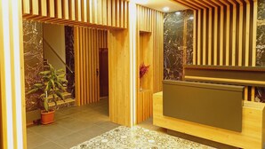 A reception area with a wooden reception desk, a potted plant, and a staircase with a marble wall. - Dinamik Otel (Sarikamis)