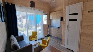 Een gezellig vakantiehuis met een zithoek, inclusief een bank en gele stoelen, een kleine keuken met houten kastjes, en een schuifdeur naar buiten.