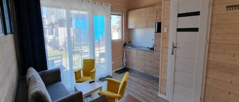 A cozy cabin with a living area featuring a sofa and yellow chairs, a small kitchen with wooden cabinets, and a sliding glass door leading to an outdoor area.
