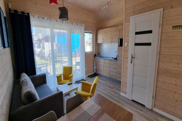 A cozy cabin with a living area featuring a sofa and yellow chairs, a small kitchen with wooden cabinets, and a sliding glass door leading to an outdoor area.