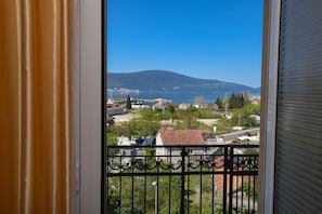 A balcony with a view of a town, a mountain, and a body of water.
