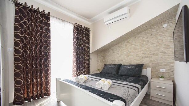 A bedroom with a bed, a nightstand, a wall-mounted air conditioner, and a window with curtains. - D&D Apartments Tivat - Apartment with 4 beds - No.11 (Tivat)