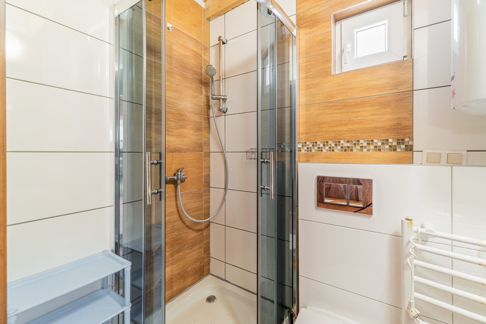 Ein modernes Badezimmer mit einer gläsernen Dusche, weißen Fliesen und einer Wand mit Holzverkleidung.