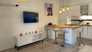 Una cocina moderna con una isla de madera, taburetes de bar, un armario blanco y un cuadro de un perro.