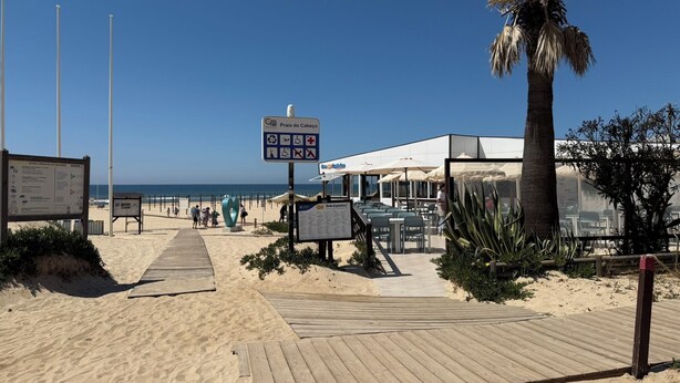 Un restaurante frente al mar con terraza al aire libre, una pasarela de madera que conduce a la playa y una vista despejada del océano.