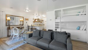 Uma sala moderna com um sofá cinza, uma área de jantar com uma cadeira branca e uma cama embutida branca com espaço de armazenamento.