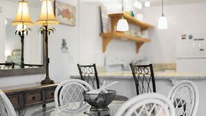 Uma sala de jantar com uma mesa redonda, cadeiras brancas e luminárias pendentes.